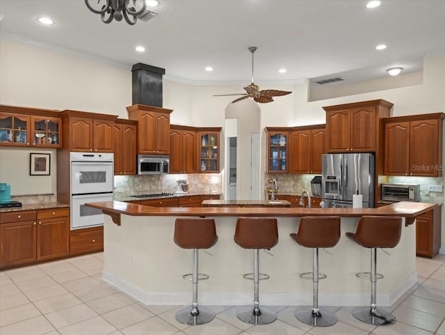 kitchen with light tile patterned flooring, appliances with stainless steel finishes, a kitchen island with sink, and a breakfast bar area