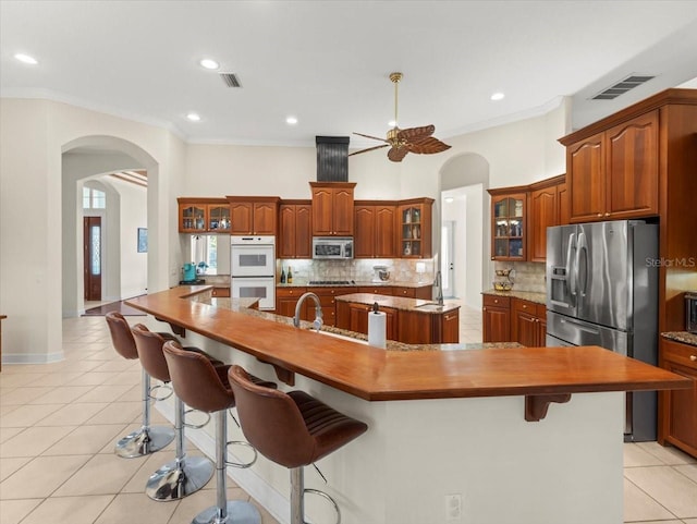 kitchen with appliances with stainless steel finishes, a kitchen bar, a kitchen island with sink, and light tile patterned floors