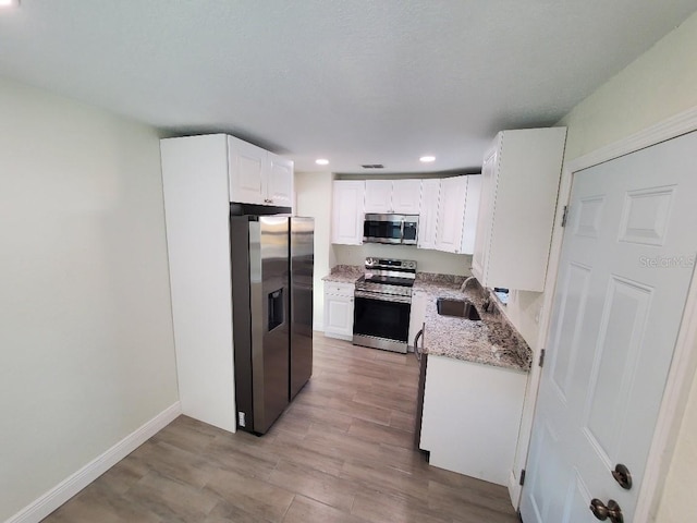 kitchen featuring appliances with stainless steel finishes, light wood-type flooring, light stone counters, white cabinets, and sink