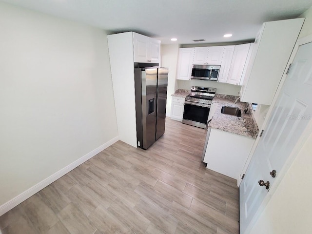 kitchen featuring appliances with stainless steel finishes, sink, light stone counters, light hardwood / wood-style floors, and white cabinets