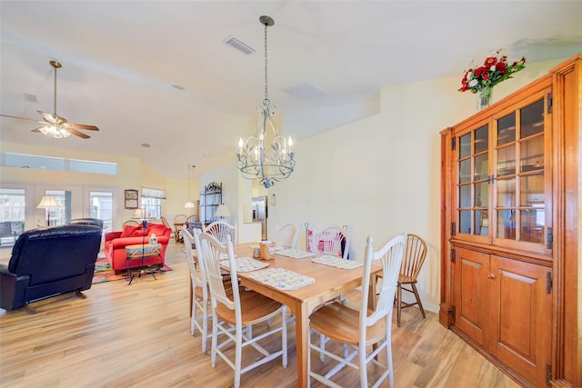 dining area with ceiling fan with notable chandelier, light hardwood / wood-style floors, and vaulted ceiling