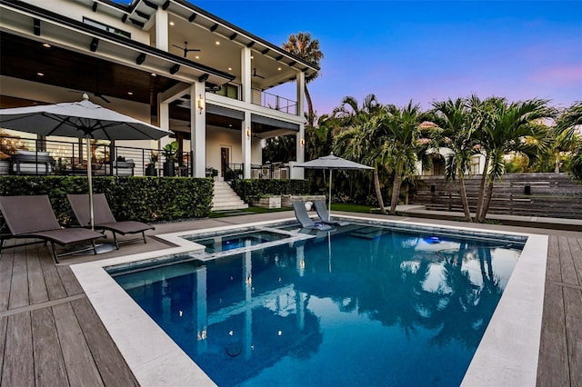 pool at dusk with ceiling fan and a pool with connected hot tub