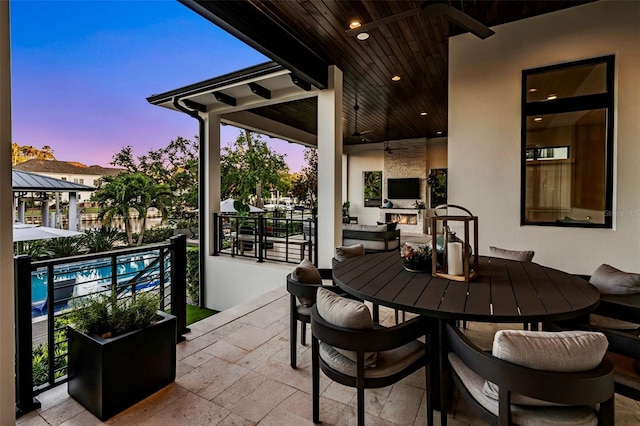 patio terrace at dusk featuring outdoor dining area, a fenced in pool, and a large fireplace