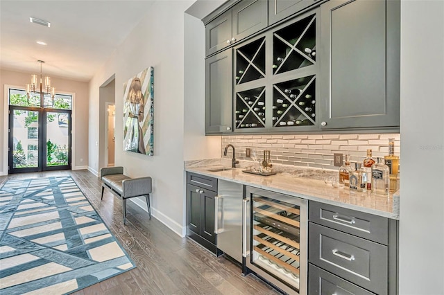 bar with wet bar, a sink, beverage cooler, decorative backsplash, and baseboards