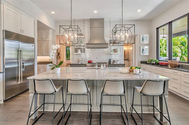 kitchen with custom exhaust hood, an inviting chandelier, a sink, and stainless steel built in fridge