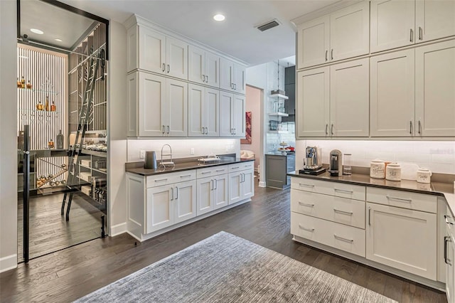 kitchen featuring tasteful backsplash, white cabinetry, dark countertops, visible vents, and dark wood finished floors