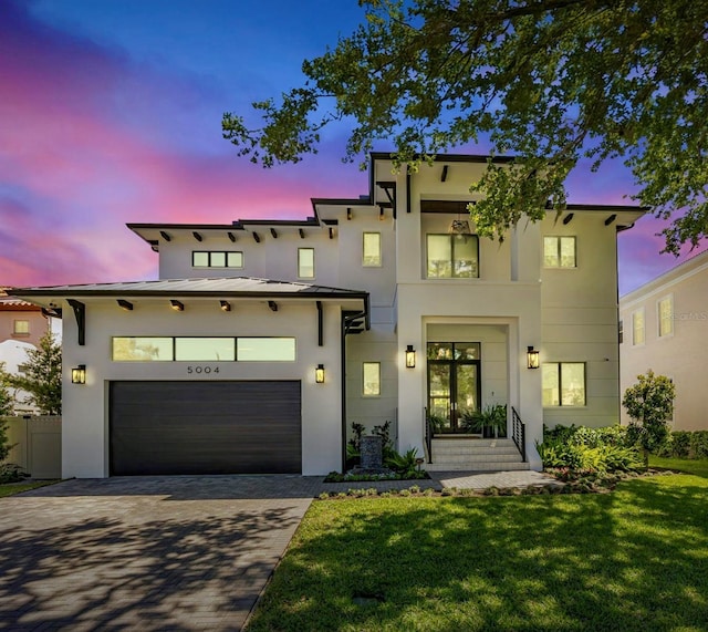 view of front of property with a garage, stucco siding, a front yard, and decorative driveway