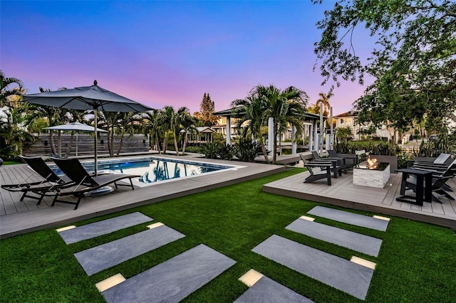 pool with a deck, a fire pit, and a lawn
