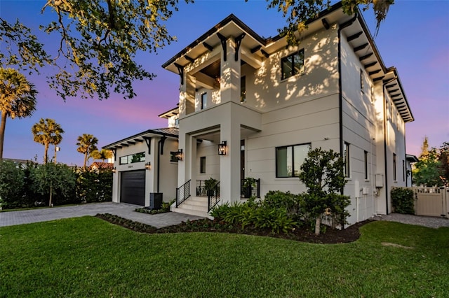 view of front of house featuring a lawn, fence, a balcony, an attached garage, and driveway
