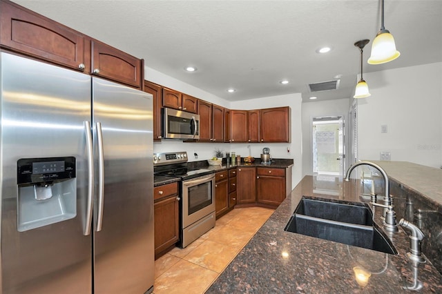 kitchen featuring light tile patterned flooring, appliances with stainless steel finishes, pendant lighting, sink, and dark stone counters