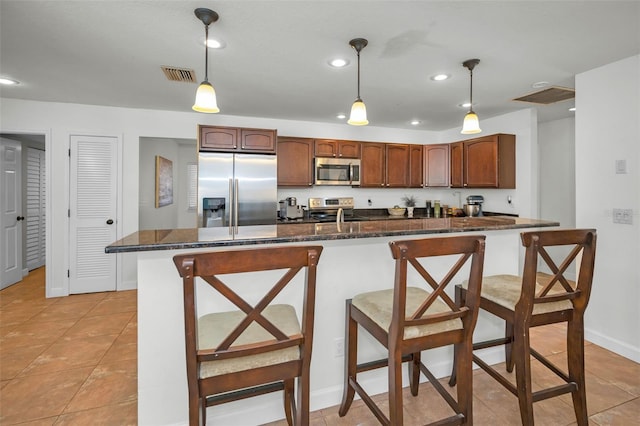 kitchen with light tile patterned flooring, appliances with stainless steel finishes, decorative light fixtures, a kitchen bar, and dark stone counters