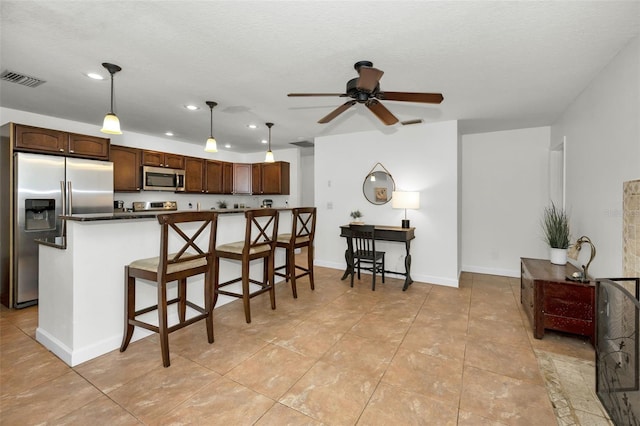 kitchen featuring a kitchen bar, dark brown cabinets, hanging light fixtures, ceiling fan, and stainless steel appliances