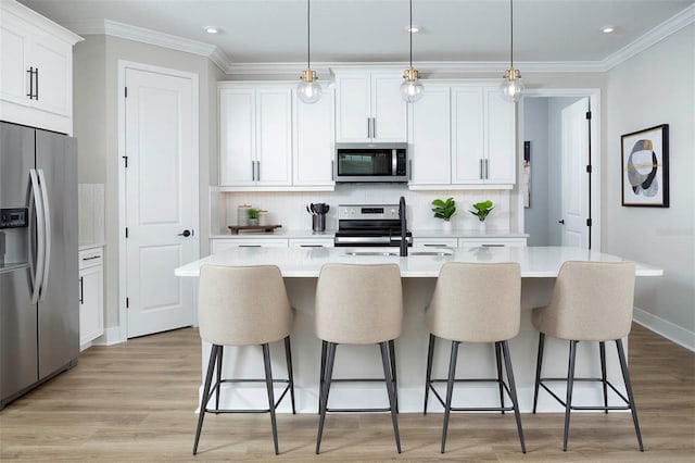 kitchen with hanging light fixtures, stainless steel appliances, an island with sink, and white cabinets