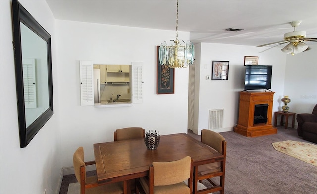 carpeted dining room featuring a fireplace, visible vents, and ceiling fan with notable chandelier