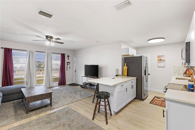 kitchen with a breakfast bar, sink, white cabinetry, light wood-type flooring, and stainless steel fridge