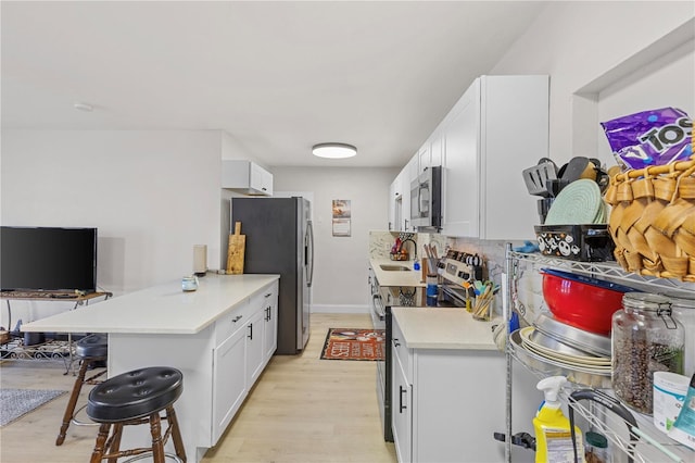 kitchen with a breakfast bar area, white cabinetry, light wood-type flooring, kitchen peninsula, and stainless steel appliances