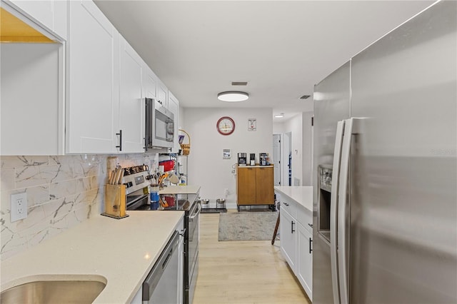 kitchen with stainless steel appliances, white cabinetry, tasteful backsplash, and light hardwood / wood-style flooring