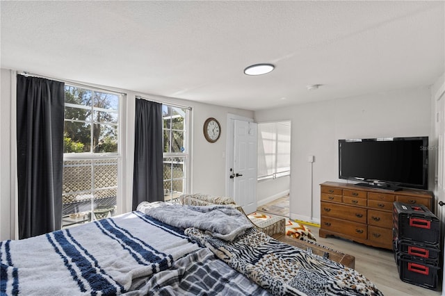 bedroom featuring access to exterior, a textured ceiling, and light hardwood / wood-style floors