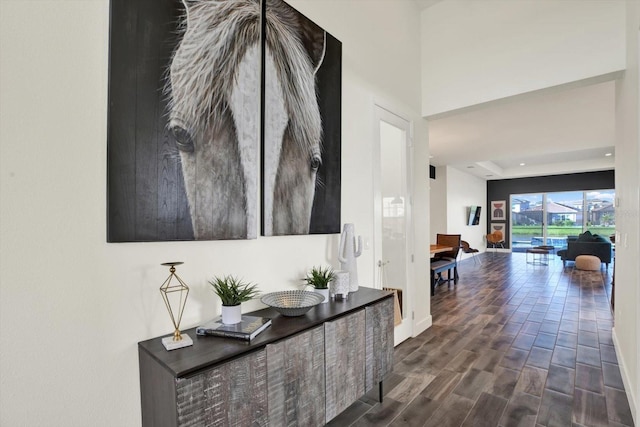 hall featuring a raised ceiling, dark wood-type flooring, and baseboards