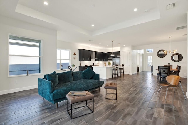 living area with a raised ceiling, visible vents, a chandelier, and wood finish floors