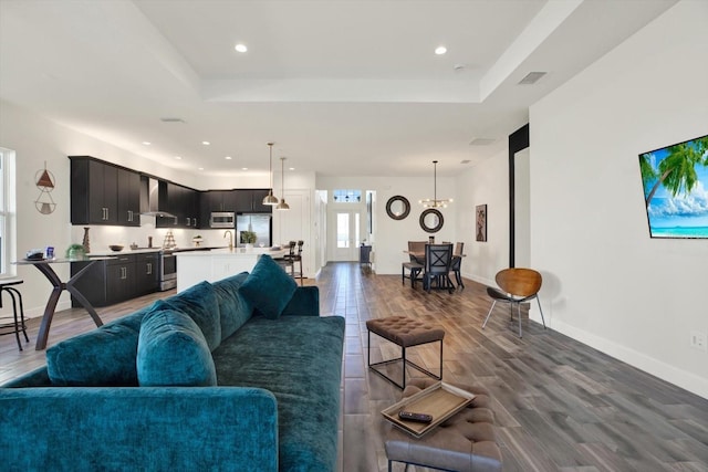 living room featuring a tray ceiling, visible vents, and dark wood-style flooring