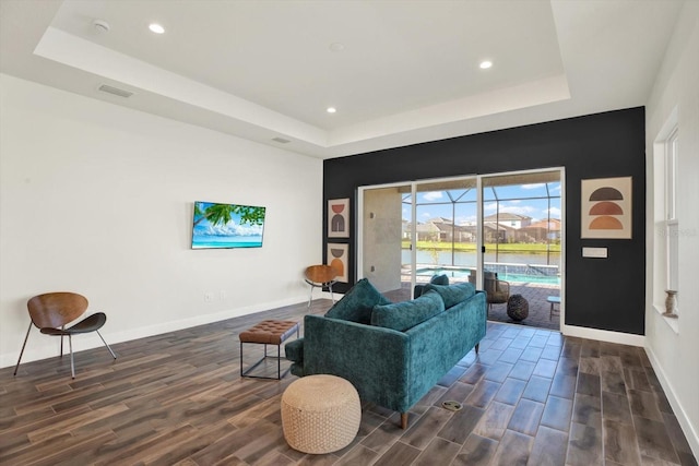 living area with dark wood finished floors, a tray ceiling, baseboards, and visible vents