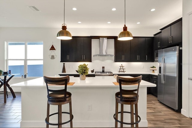 kitchen featuring visible vents, appliances with stainless steel finishes, a breakfast bar area, wall chimney exhaust hood, and light countertops