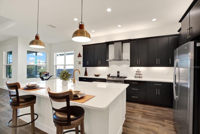 kitchen featuring stainless steel appliances, dark cabinetry, light countertops, and wall chimney range hood