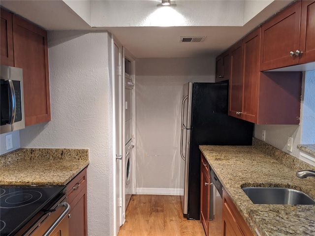 kitchen with appliances with stainless steel finishes, sink, stacked washer / drying machine, light stone counters, and light hardwood / wood-style floors