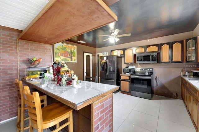 1011 W Columbus Dr, Tampa, FL 33602 - kitchen featuring brown cabinetry, stainless steel appliances, light tile patterned flooring, a ceiling fan, and a kitchen breakfast bar