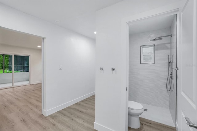 bathroom with toilet, hardwood / wood-style floors, and a tile shower