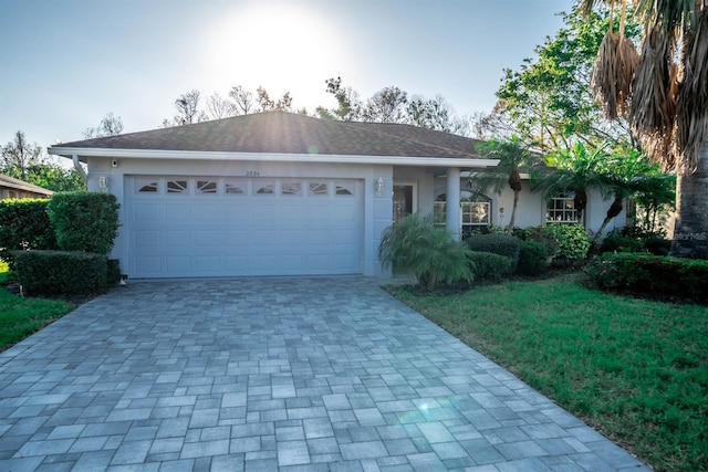 single story home featuring decorative driveway, an attached garage, a front yard, and stucco siding