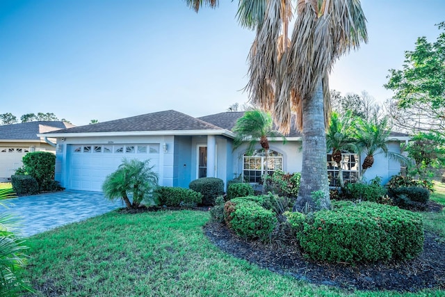 ranch-style home featuring decorative driveway, stucco siding, a shingled roof, a garage, and a front lawn