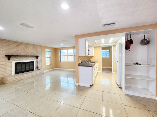 kitchen featuring light tile patterned floors, dark countertops, visible vents, freestanding refrigerator, and a brick fireplace