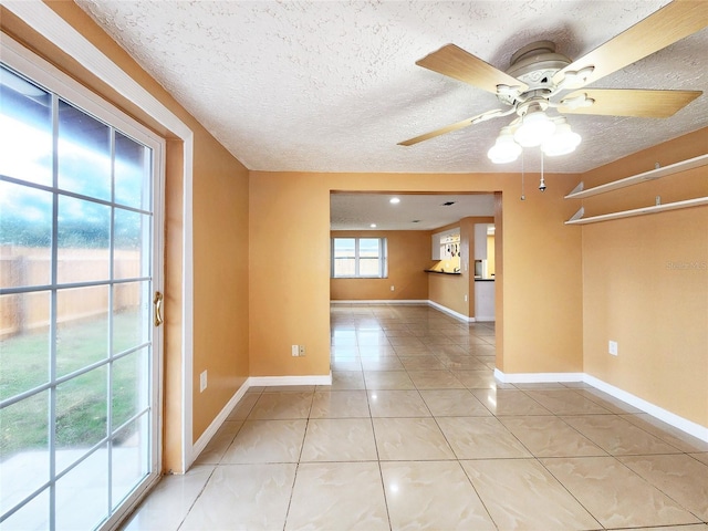 spare room featuring a ceiling fan, a textured ceiling, baseboards, and light tile patterned floors