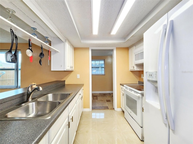 kitchen featuring dark countertops, white appliances, white cabinetry, and a sink