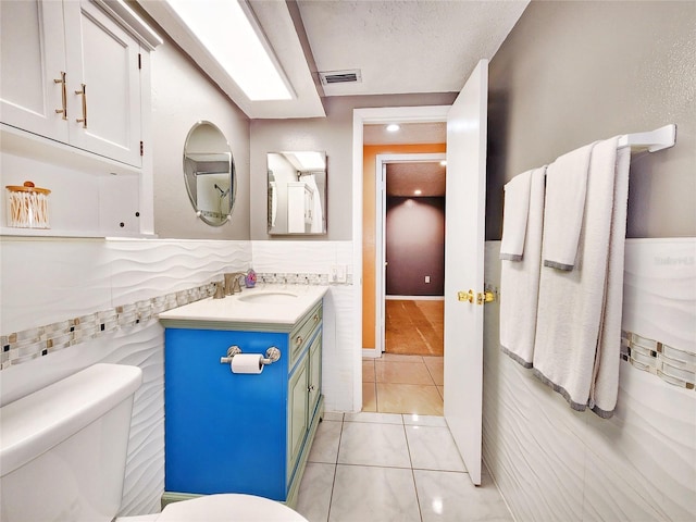 bathroom with tile patterned flooring, toilet, vanity, visible vents, and tile walls