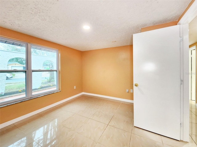 spare room with baseboards, a textured ceiling, and light tile patterned flooring