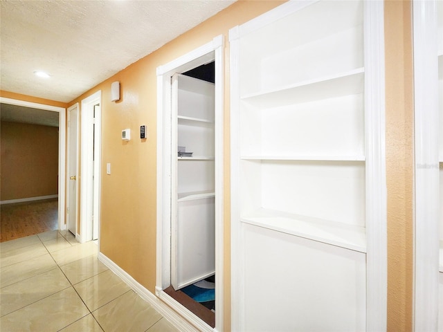 corridor with light tile patterned floors, baseboards, and a textured ceiling