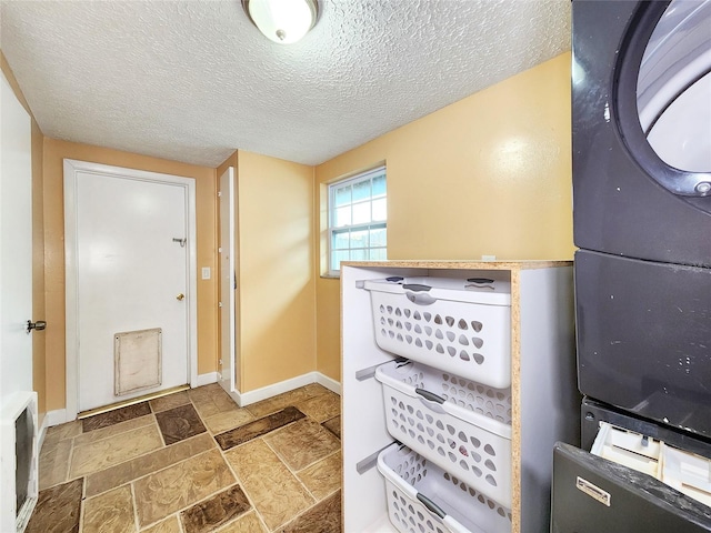 entryway featuring stacked washer / dryer, stone tile flooring, a textured ceiling, and baseboards