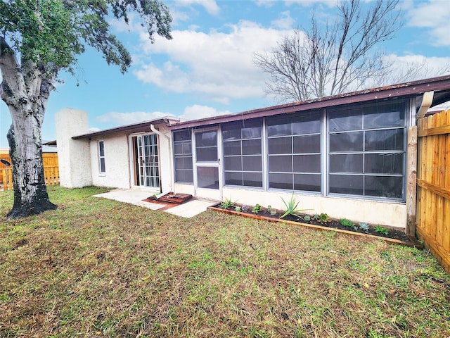 rear view of house with a lawn, fence, a sunroom, and stucco siding