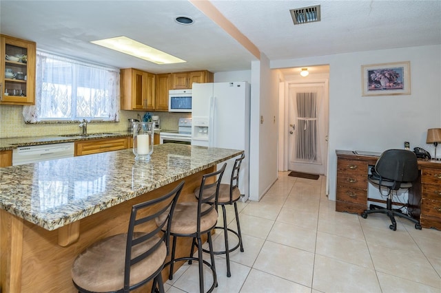 kitchen featuring sink, white appliances, light tile patterned floors, light stone countertops, and a kitchen bar