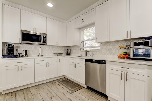 kitchen with tasteful backsplash, appliances with stainless steel finishes, light countertops, white cabinetry, and a sink