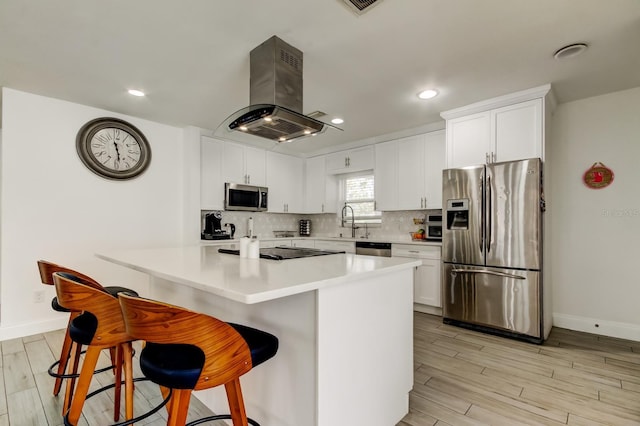 kitchen featuring stainless steel appliances, tasteful backsplash, island range hood, light wood-type flooring, and a kitchen bar