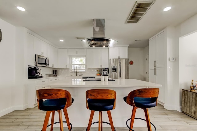 kitchen with island range hood, visible vents, appliances with stainless steel finishes, a sink, and backsplash