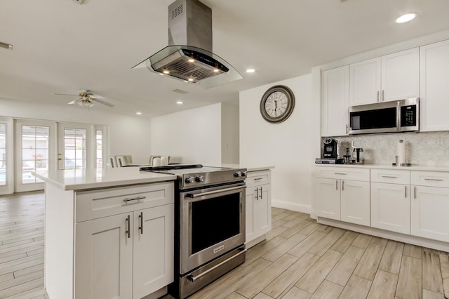 kitchen with island range hood, light countertops, appliances with stainless steel finishes, light wood-type flooring, and backsplash