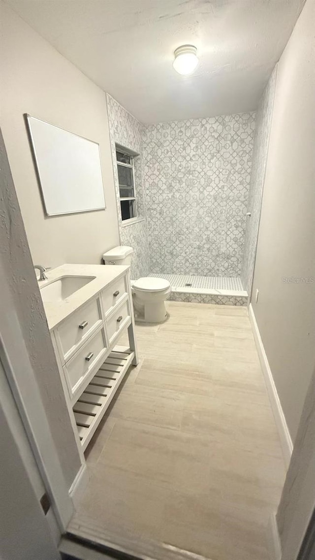 bathroom featuring toilet, wood finished floors, vanity, baseboards, and a shower stall