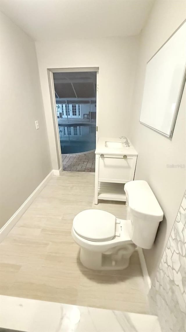 bathroom with toilet, a sink, baseboards, and wood finished floors