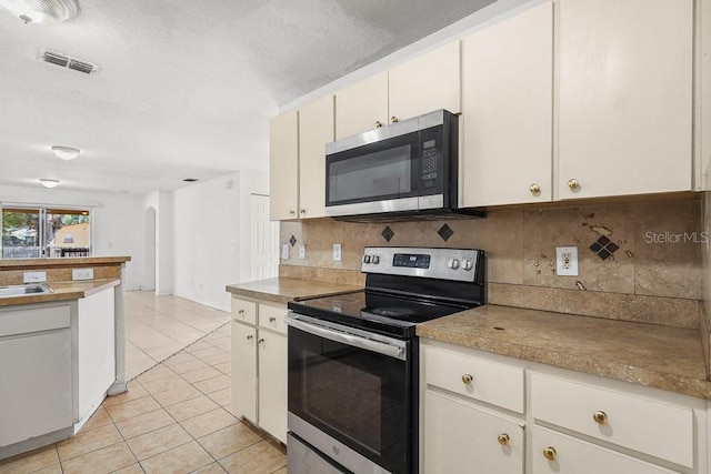 kitchen with white cabinetry, backsplash, light tile patterned flooring, and appliances with stainless steel finishes