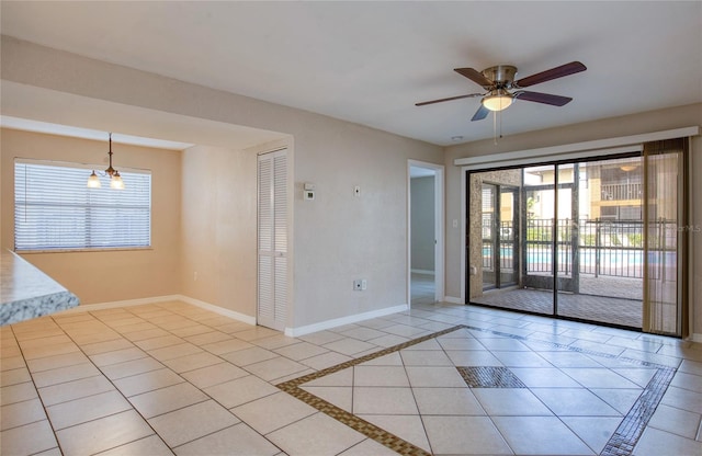 tiled spare room with ceiling fan with notable chandelier